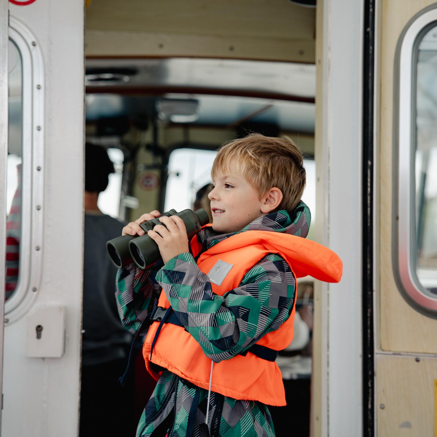 Jongetje met reddingsvest aan op een rondvaartboot met een verrekijker
