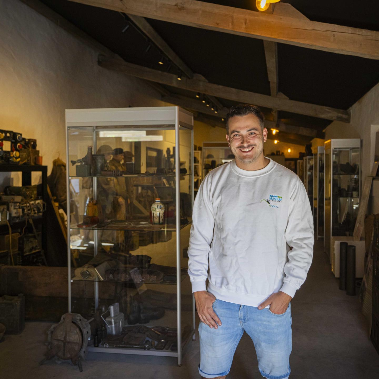 Rik staat in het ScheldeSlag Museum Biervliet voor een vitrinekast met allerlei oude oorlogsspullen.