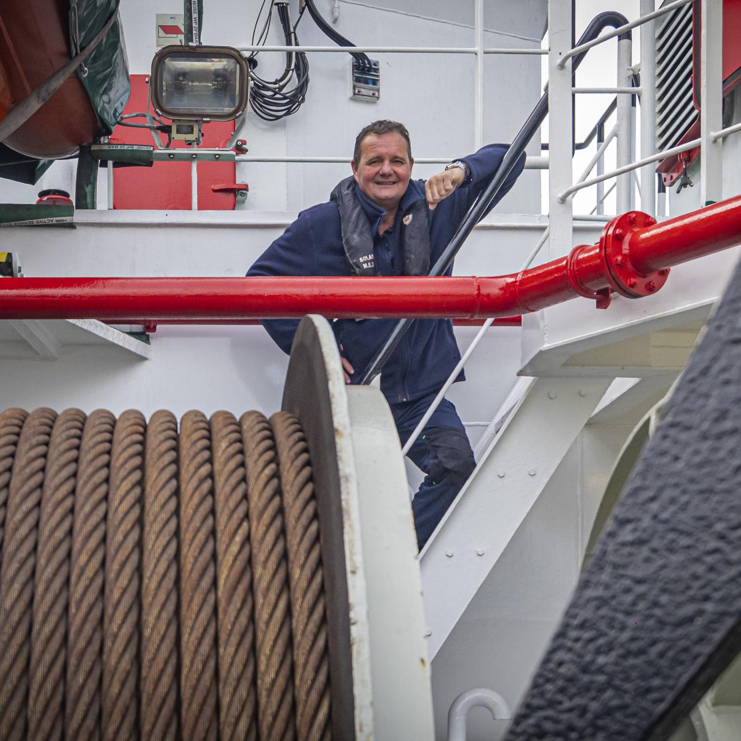 Schipper Bertus poseert voor de foto op een stalen trap van het schip met op de voorgrond een rol scheepstouw