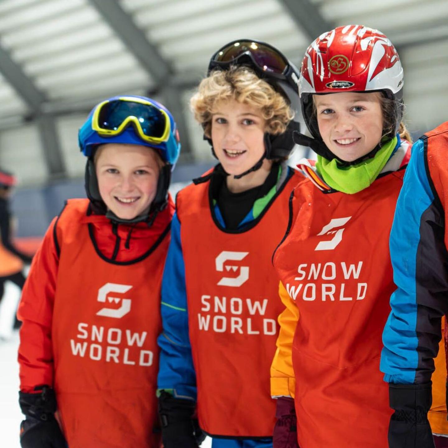 Drie vrolijke kinderen poseren schouder aan schouder tijdens skiles bij SnowWorld Terneuzen