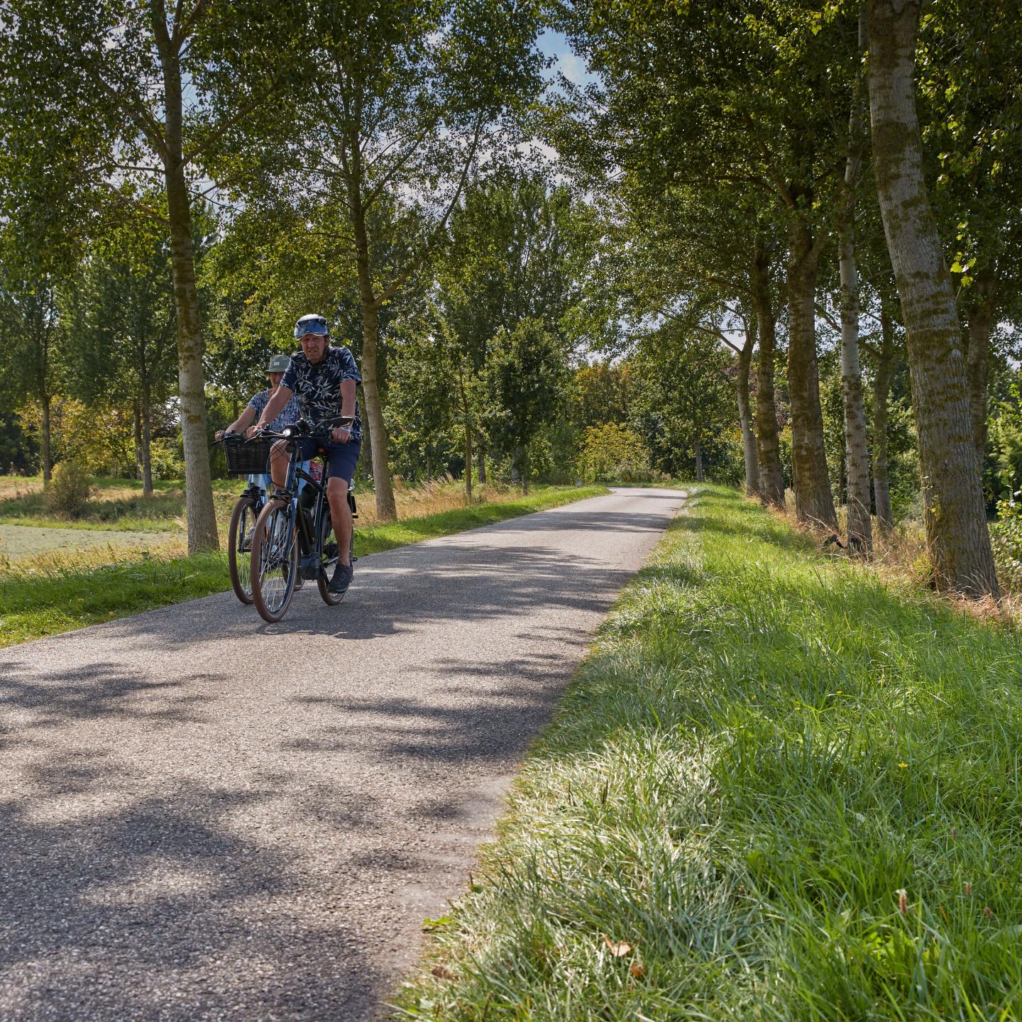 Twee mensen fietsen over een lage dijk in de polder