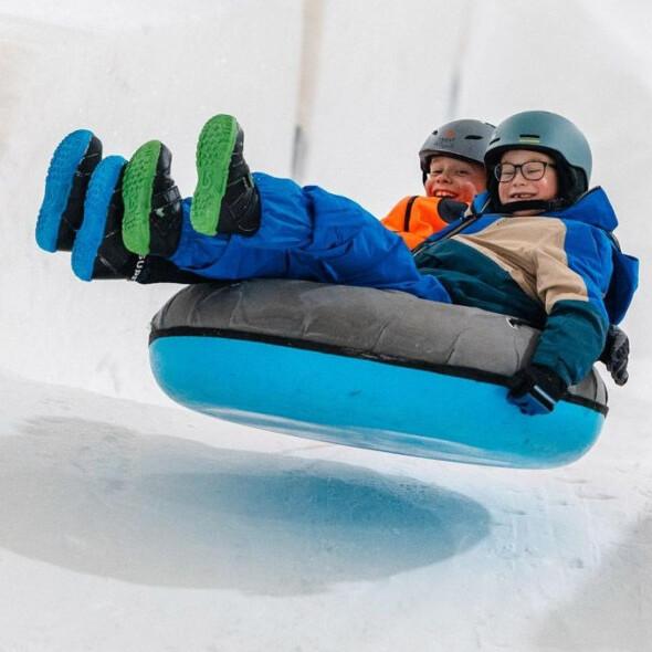 Twee blije kinderen sjezen een skipiste af in een opblaasband