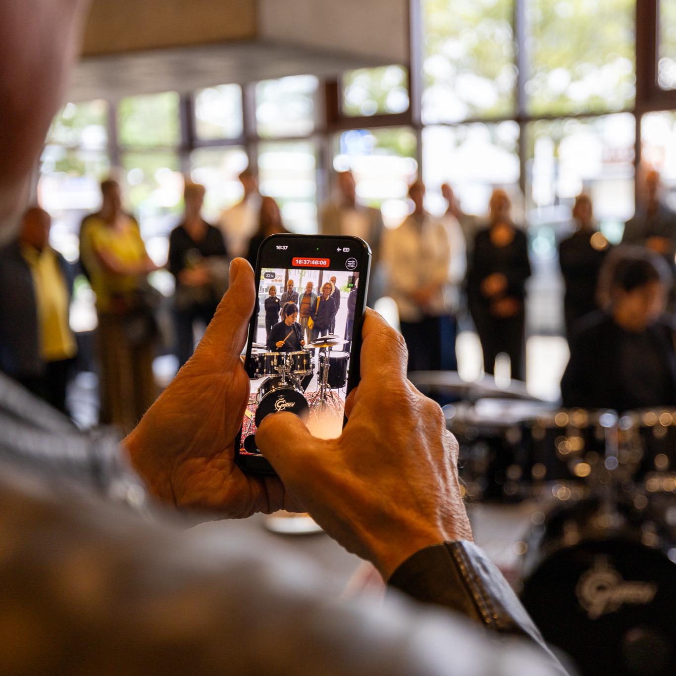 Man filmt drummer en publiek op de achtergrond met zijn mobiel