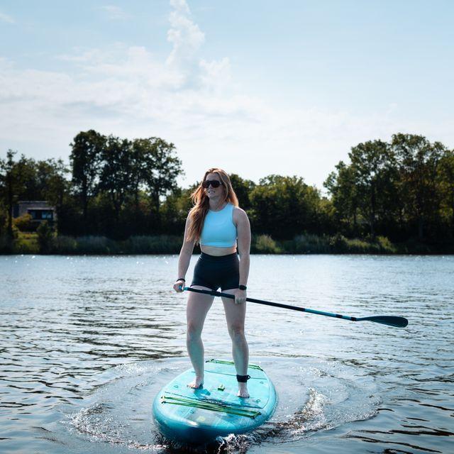 Meisje staat op blauw supboard in het water met peddel in de hand en mooie natuur op de achtergrond