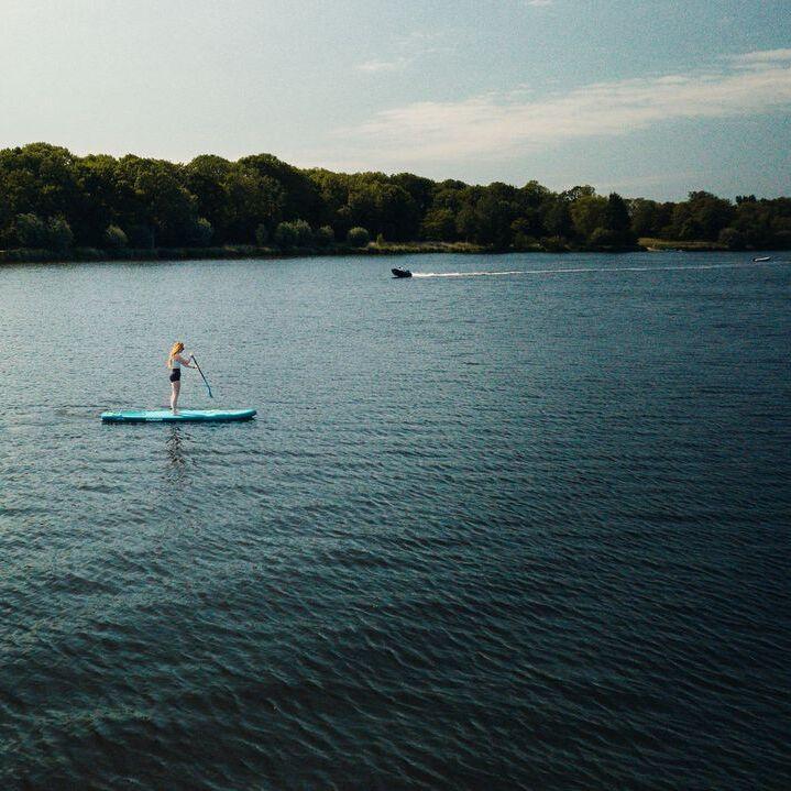 Meisje op suboard op een grote kreek met bossen op de achtergrond