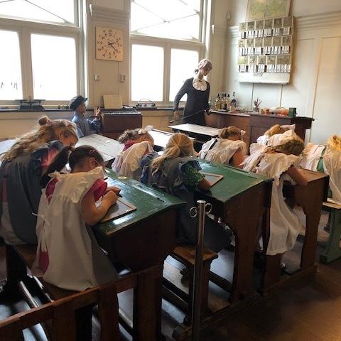 Kinderen in Schooltijd museum zitten te schrijven aan authentieke schoolbureaus