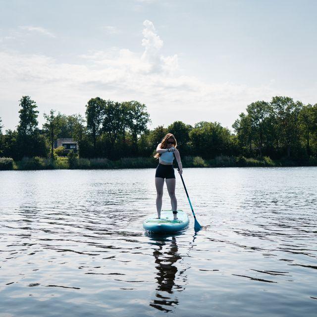 Meisje op suboard op een grote kreek met bossen op de achtergrond