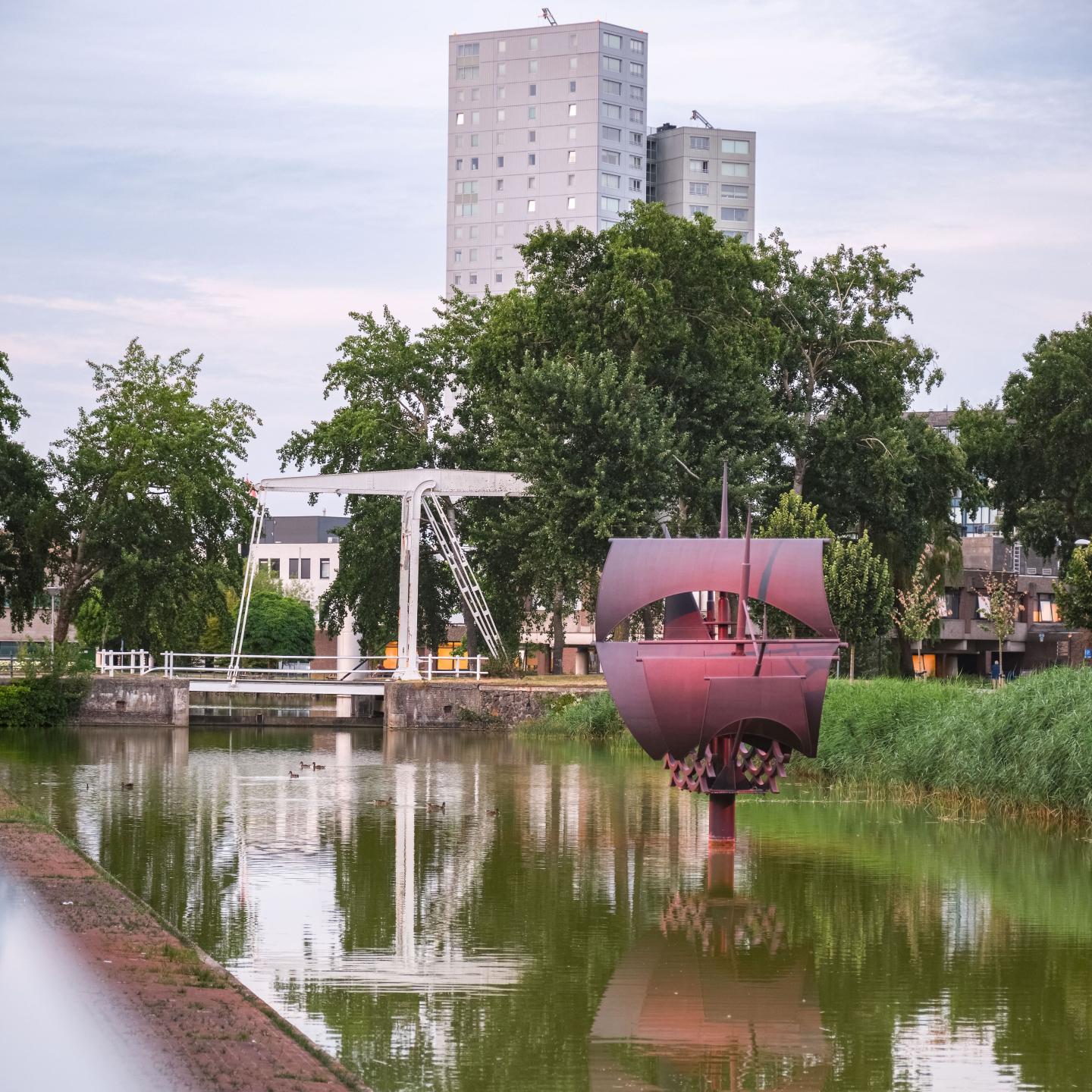 kunstwerk de vliegende hollander met op de achtergrond een loopbrug en groot appartementencomplex