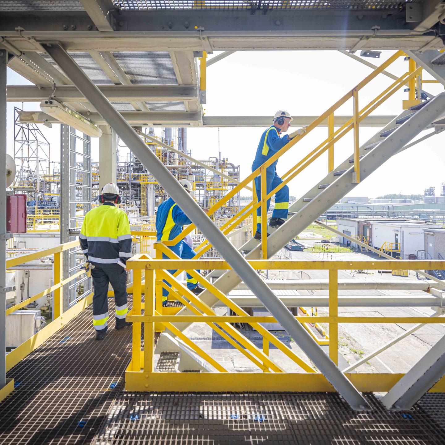 JPP-begeleider Etienne loopt een stalen trap op bij Dow Terneuzen met studenten die hem volgen en industrie op de achtergrond