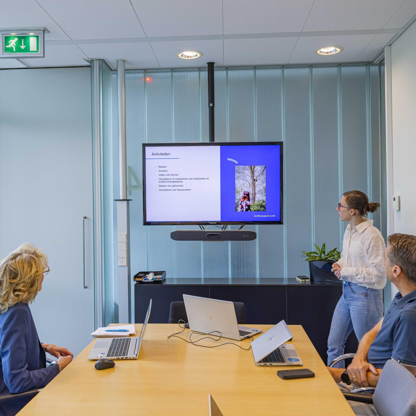 Lieke presenteert iets op een groot scherm in een vergaderruimte met twee personen die daarnaar kijken