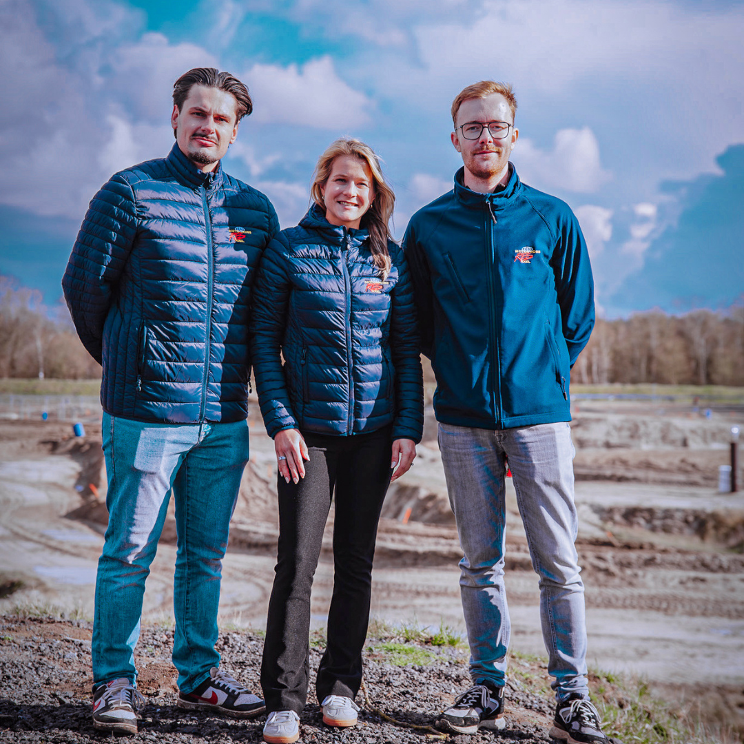Evie poseert op het crossterrein met twee mede bestuursleden links en rechts van haar