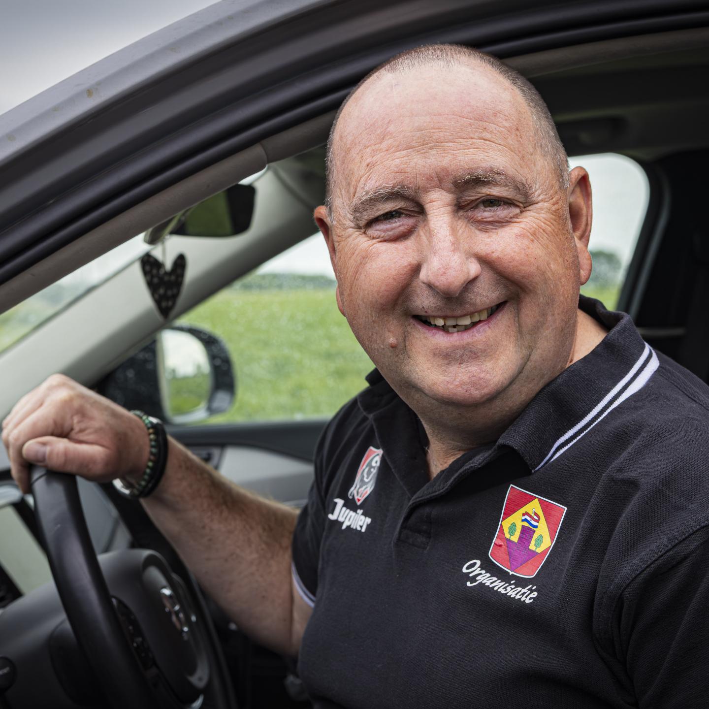 Martin achter het stuur van zijn auto breed glimlachend in de camera