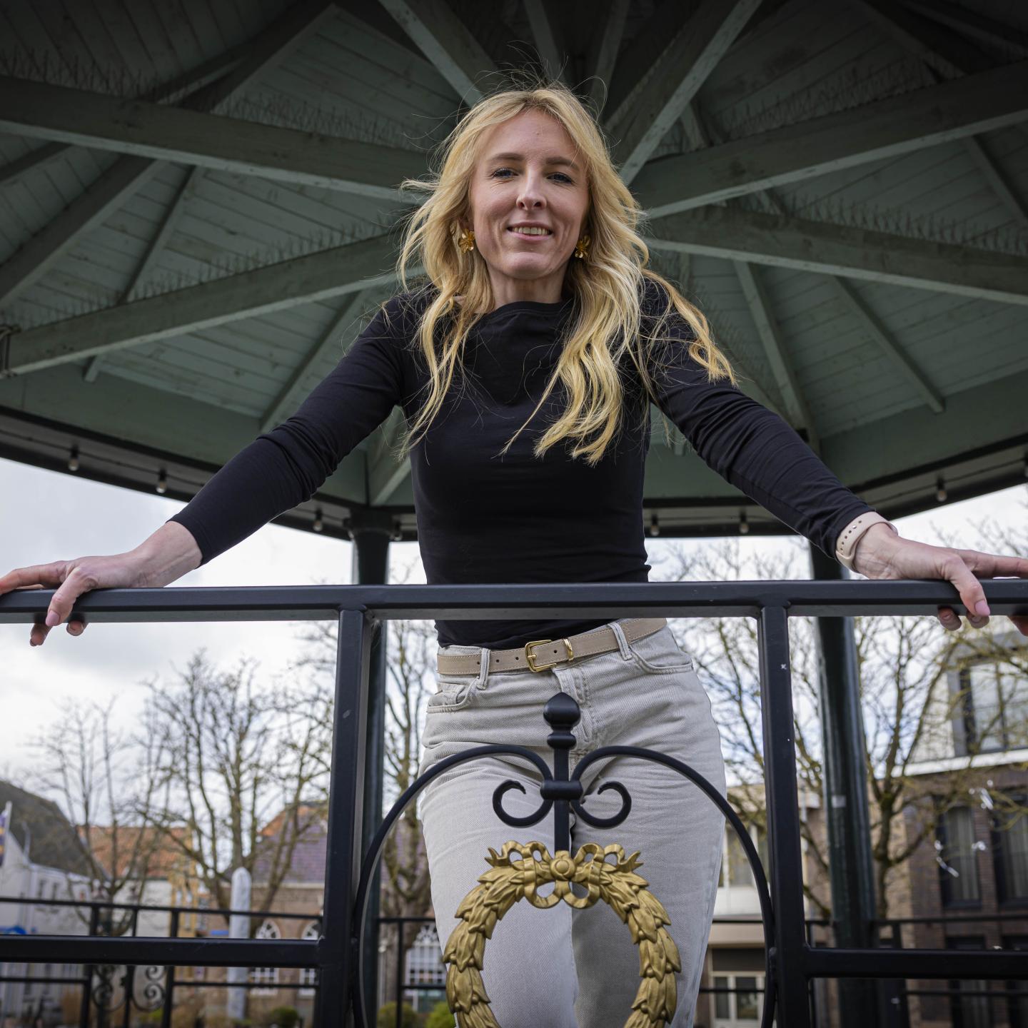 Michelle leunt tegen de reling van de kiosk op het plein in Philippine en kijkt in de camera die beneden op haar gericht staat