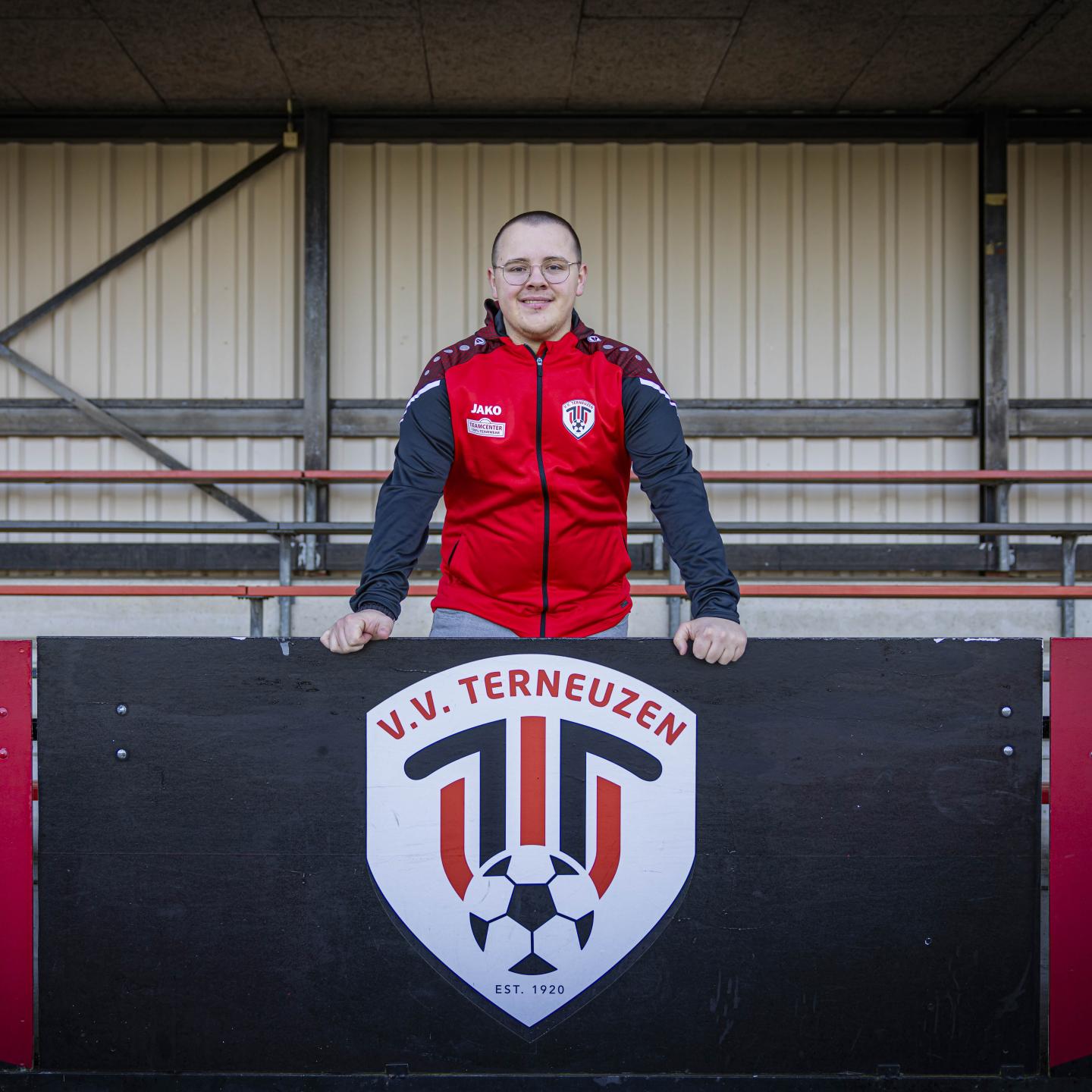 Wouter poseert voor de camera op de tribune bij het embleem van VV Terneuzen
