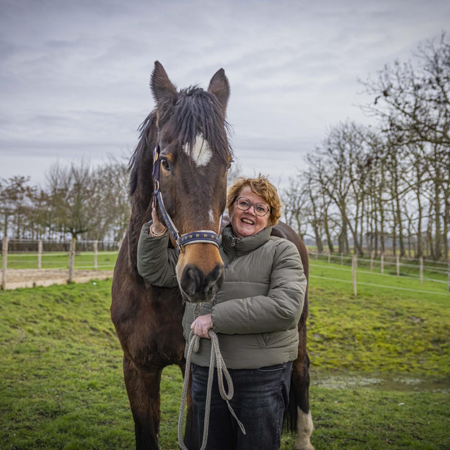 Heleen poseert in de wei met een bruin paard