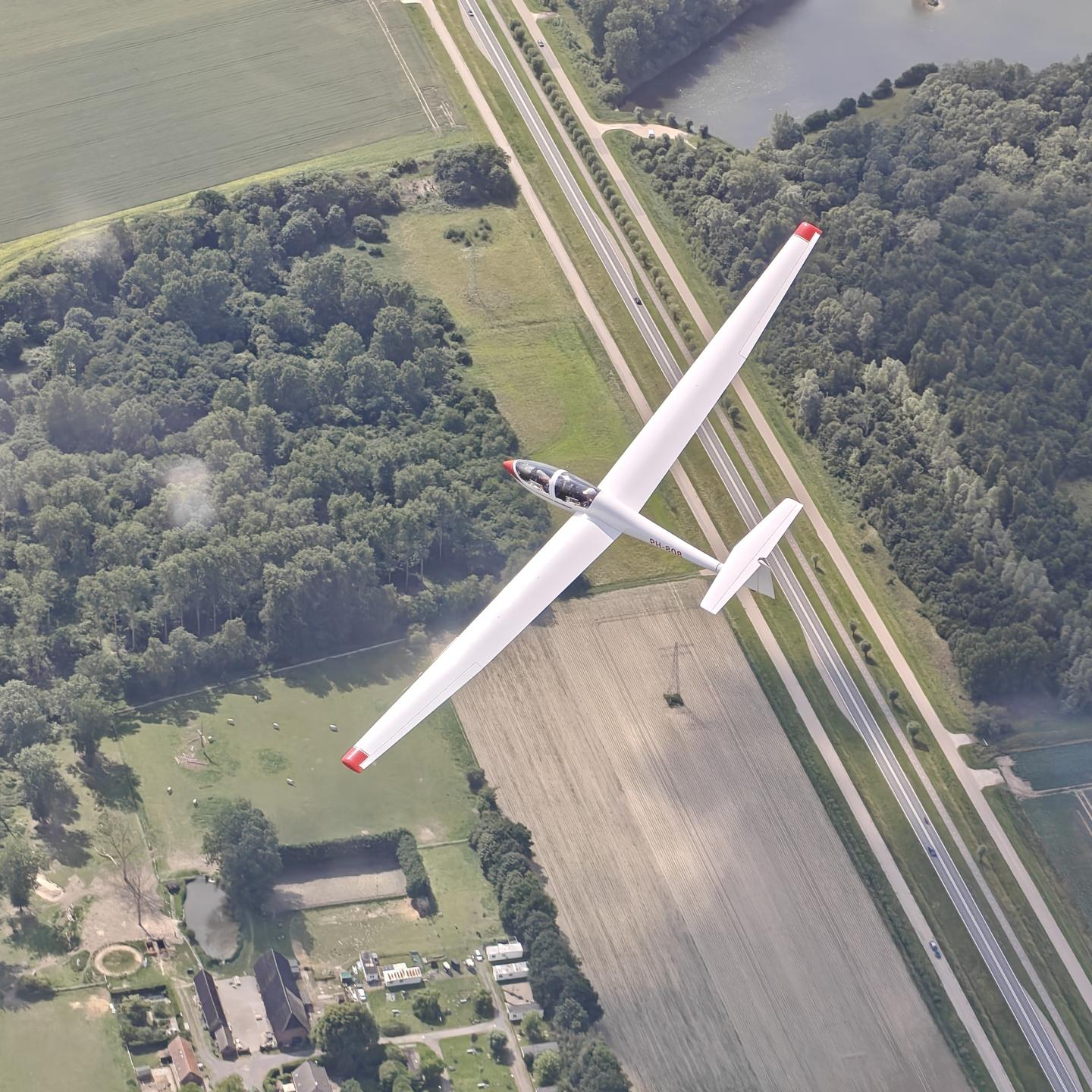 Zweefvliegtuig van bovenaf gefotografeerd met daaronder een weids uitzicht over de polder
