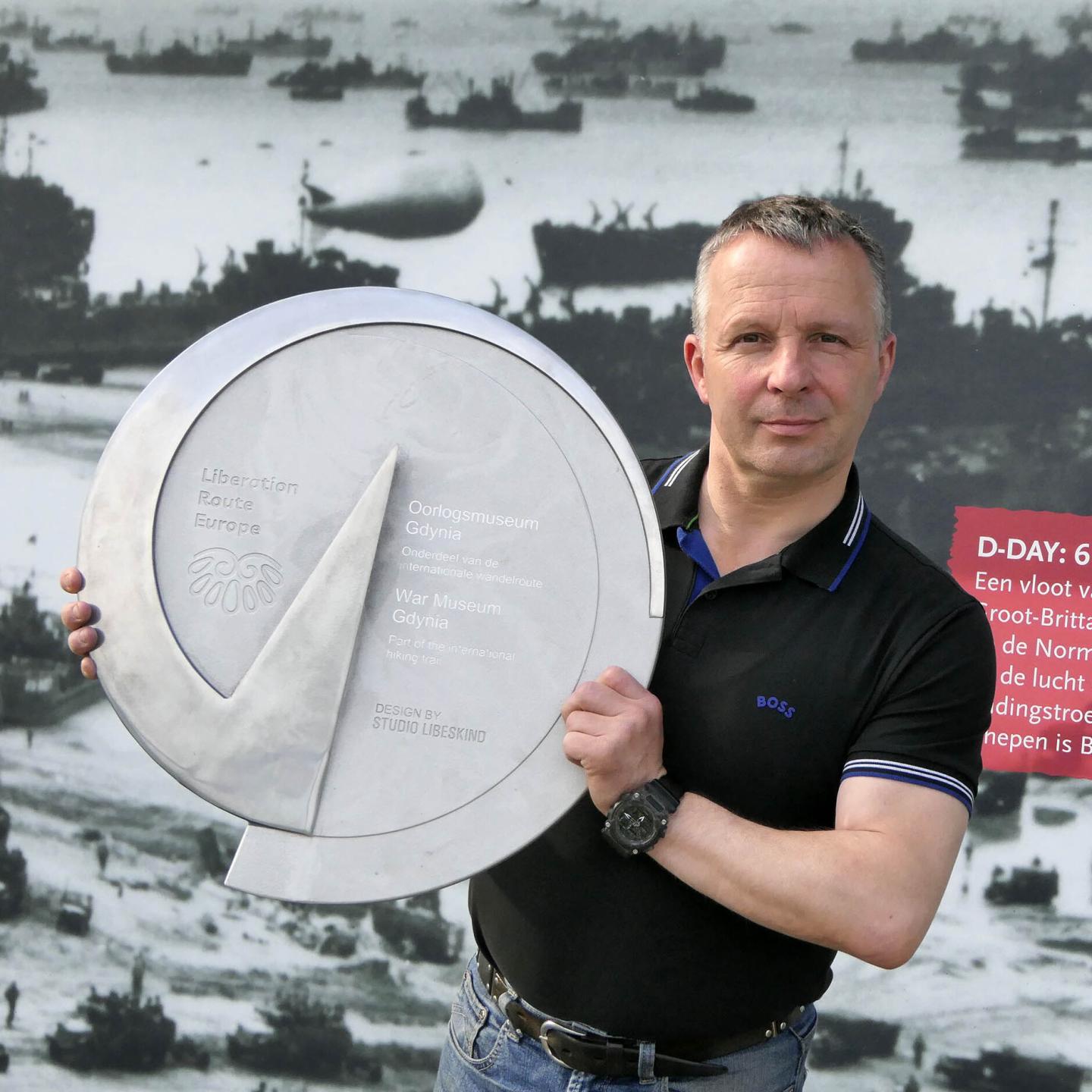 Museumoprichter Mario met een groot rond plakkaat van D-Day in zijn handen