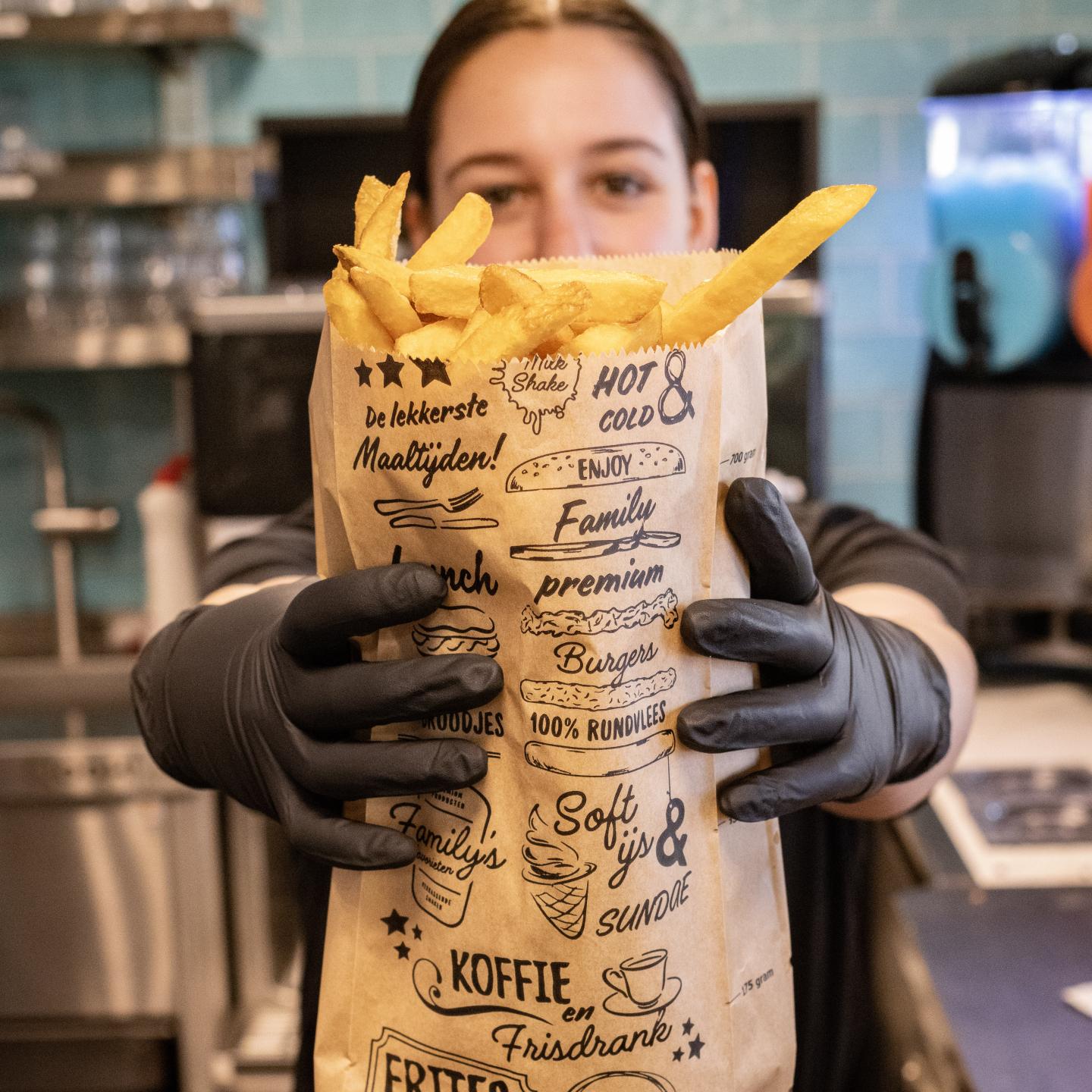 Medewerkster houdt grote zak frites voor de fotocamera