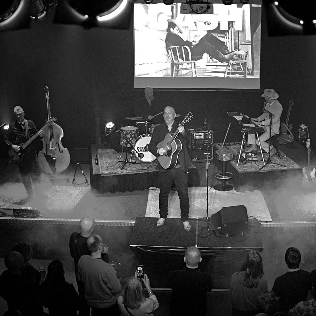 Zwart wit foto van zanger, bassist en pianist op het podium van de pit