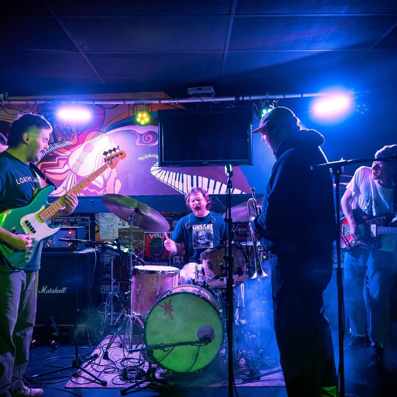 Drummer gaat helemaal uit zijn dak achter zijn drumstel met om hem heen gitaarspelende bandleden