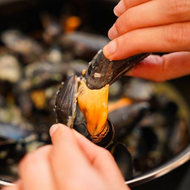 Twee handen die met een mosselschelp een mossel uit een andere mosselschelp halen