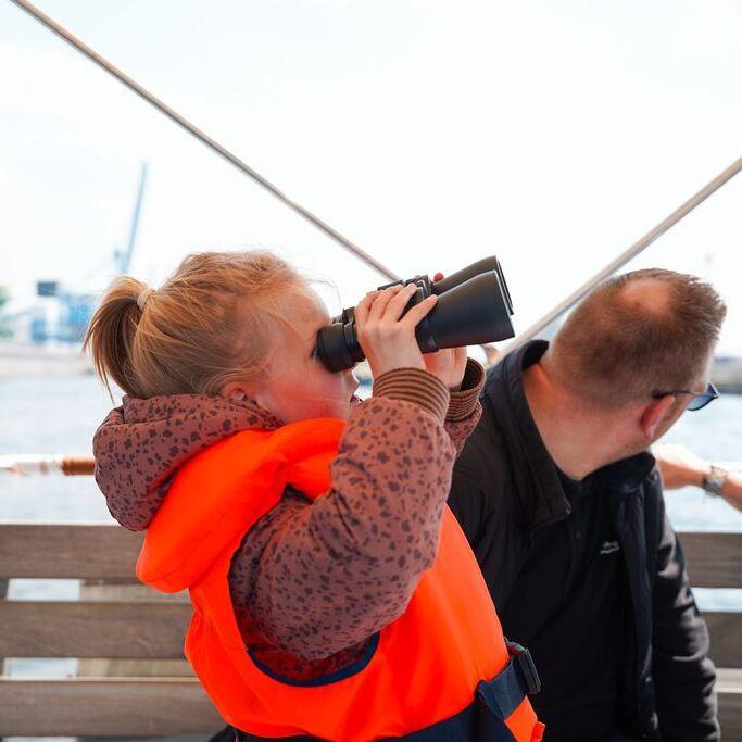Jong meisje met reddingsvest aan op een rondvaartboot kijkt door een verrekijker