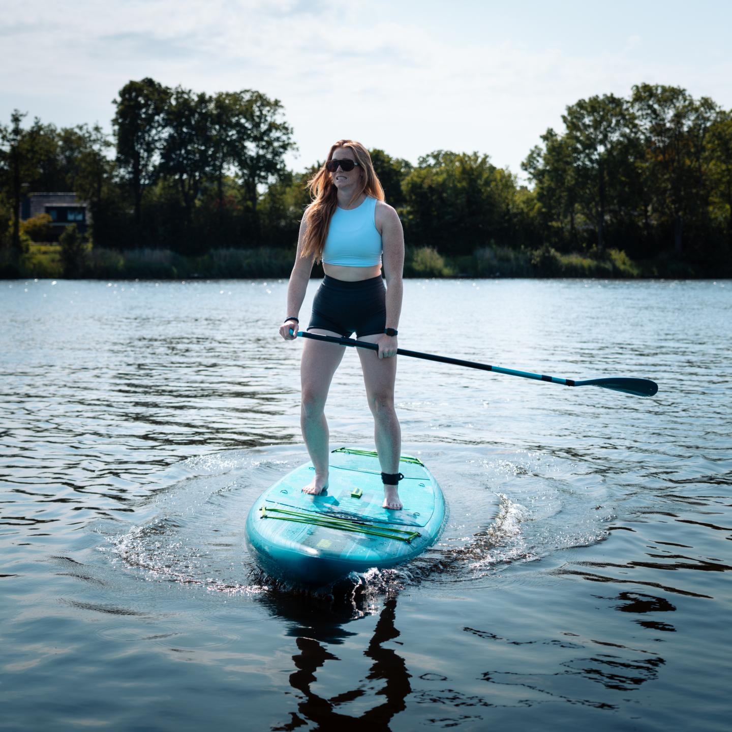 Meisje staat op blauw supboard in het water met peddel in de hand en mooie natuur op de achtergrond