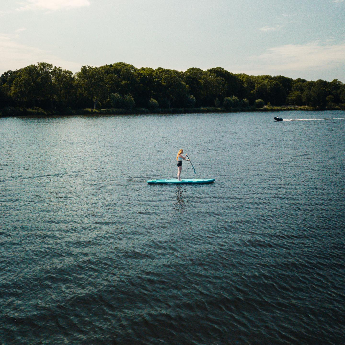 Meid op een sup op de kreek met de skyline van Terneuzen erachter